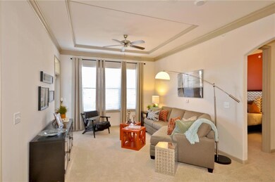 Carpeted living room featuring ceiling fan, a tray ceiling, and ornamental molding