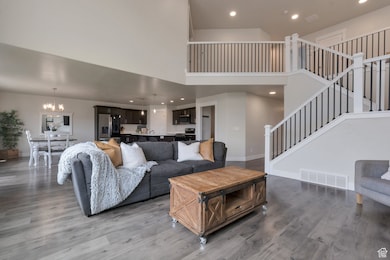 Living room with stairway, wood finished floors, visible vents, an inviting chandelier, and a towering ceiling