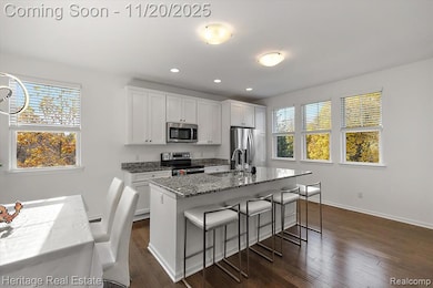 Kitchen featuring light stone counters, a breakfast bar area, white cabinets, appliances with stainless steel finishes, and a center island with sink