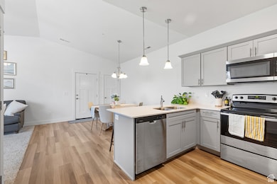 Kitchen with stainless steel appliances, gray cabinets, decorative light fixtures, a kitchen bar, and light wood-style floors