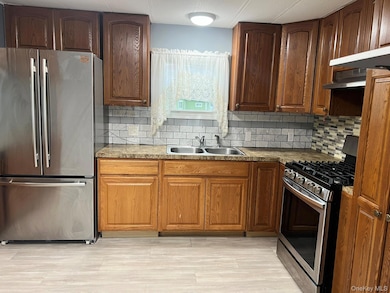 Kitchen with stainless steel appliances, decorative backsplash, light wood-style flooring, and under cabinet range hood