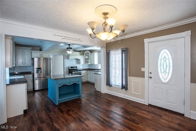 Entrance foyer with a chandelier, crown molding, a textured ceiling, dark wood-style floors, and ceiling fan