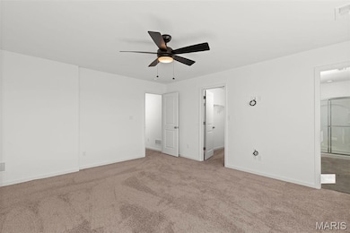 Unfurnished bedroom featuring light carpet, a walk in closet, ensuite bathroom, ceiling fan, and a closet