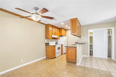 Kitchen with white electric stove, brown cabinetry, light tile patterned flooring, a textured ceiling, and dark stone counters