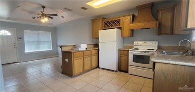 Kitchen featuring white appliances, a sink, a tray ceiling, custom range hood, and a peninsula