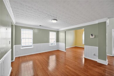 Empty room with light wood-style floors, crown molding, a wainscoted wall, and a textured ceiling