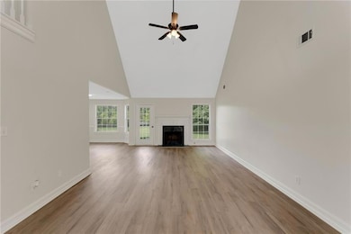 Unfurnished living room with a towering ceiling, baseboards, wood finished floors, a premium fireplace, and ceiling fan