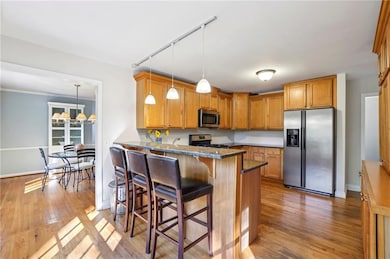 Kitchen with stainless steel appliances, track lighting, brown cabinetry, hanging light fixtures, and a peninsula