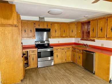 Kitchen featuring appliances with stainless steel finishes, light wood finished floors, under cabinet range hood, and brown cabinetry