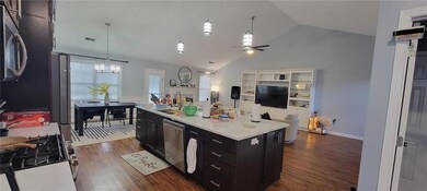 Kitchen with dark cabinetry, dishwasher, vaulted ceiling, dark wood-type flooring, and a ceiling fan