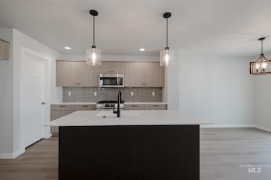 Kitchen with decorative light fixtures, tasteful backsplash, an island with sink, light stone counters, and stainless steel appliances