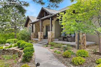 Property entrance featuring stucco siding, covered porch, stone siding and exquisite landscaping.