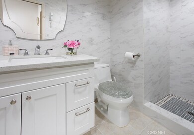 Sumptuous newly remodeled guest bathroom with modern white vanity, designer dressing mirror, marble tiled walls, frameless glass enclosed marble tiled shower with custom tiled floor and decorative inlay.
