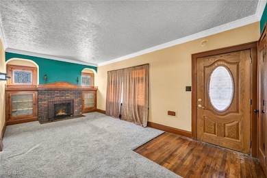Foyer entrance featuring crown molding, a textured ceiling, a brick fireplace, dark carpet, and dark wood finished floors