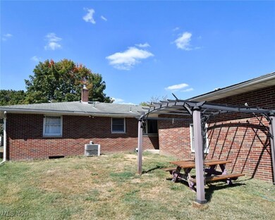 Rear view of house featuring brick siding, a pergola, a yard, and a chimney