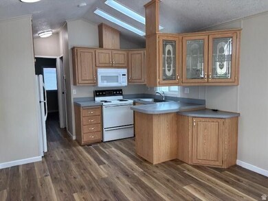 Kitchen with white appliances, glass insert cabinets, lofted ceiling, dark wood finished floors, and brown cabinets