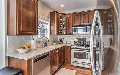 Kitchen featuring stainless steel appliances, light stone countertops, backsplash, light wood-style flooring, and glass insert cabinets