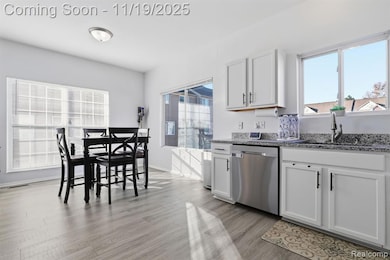 Kitchen featuring white cabinets, dark stone countertops, dishwasher, and light wood finished floors