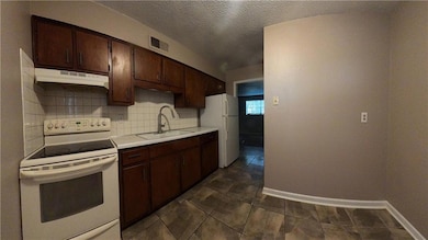 Kitchen featuring white appliances, dark brown cabinets, a textured ceiling, light countertops, and decorative backsplash
