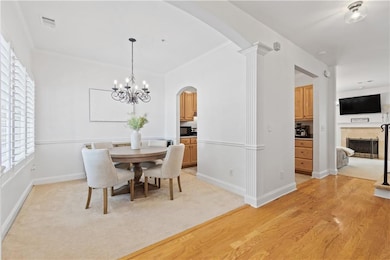 Dining area with arched walkways, a fireplace, a chandelier, vaulted ceiling, and light wood-style floors