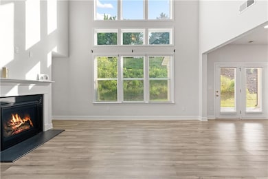 Unfurnished living room with a high ceiling, a lit fireplace, light wood finished floors, and baseboards