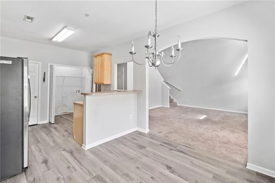 Kitchen featuring freestanding refrigerator, light brown cabinetry, a chandelier, light wood-style floors, and arched walkways