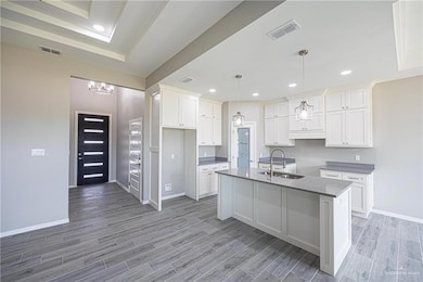 Corridor featuring a raised ceiling, light marble finish flooring, and a chandelier