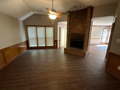 Unfurnished living room with wainscoting, a brick fireplace, a ceiling fan, a decorative wall, and lofted ceiling