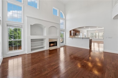 Unfurnished living room with a fireplace with flush hearth, dark wood-style flooring, built in shelves, a towering ceiling, and arched walkways