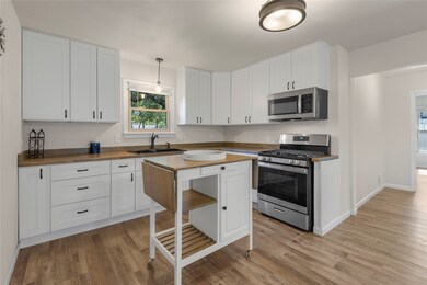 Kitchen featuring appliances with stainless steel finishes, butcher block countertops, white cabinetry, and decorative light fixtures