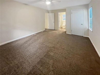 Unfurnished bedroom with dark carpet, ensuite bath, and ceiling fan