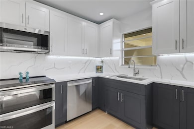 Kitchen with white cabinets, light stone countertops, stainless steel appliances, tasteful backsplash, and a sink