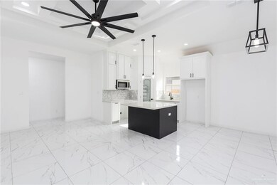 Kitchen featuring pendant lighting, ceiling fan with notable chandelier, light tile floors, a center island, and white cabinetry