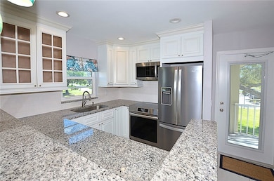 Kitchen with light stone counters, appliances with stainless steel finishes, white cabinetry, glass insert cabinets, and tasteful backsplash