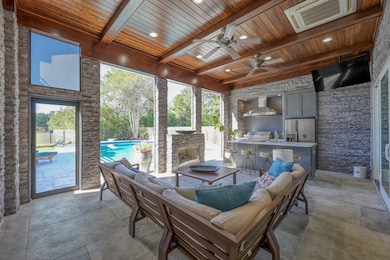 This stunning outdoor kitchen and living space is perfect for entertaining year-round. Featuring sleek stone accents, a wood-paneled ceiling with recessed lighting and fans, and a built-in grill with bar seating, it combines luxury and functionality. Automatic shades provide comfort and privacy at the touch of a button, while the cozy seating area and fireplace overlook a sparkling pool for the ultimate indoor-outdoor experience.