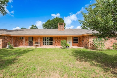 Charming single-story brick home with a spacious front lawn and covered entryway. Features a central chimney, large windows, and mature trees, creating a welcoming, private atmosphere.