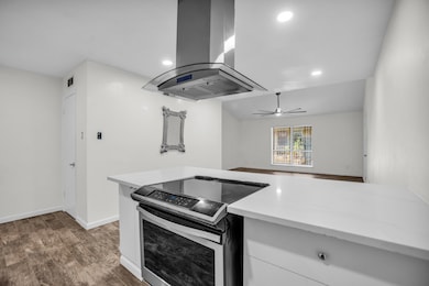 Kitchen with stainless steel electric stove, island range hood, light stone countertops, white cabinets, and dark wood-style flooring