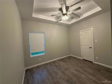 Empty room with dark hardwood / wood-style flooring, ceiling fan, and a raised ceiling