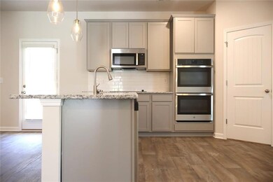 Kitchen with stainless steel appliances, gray cabinets, decorative backsplash, dark wood-style floors, and light stone counters