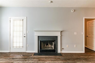 Detailed view of wood finished floors, a fireplace with flush hearth, a smoke detector, and a textured ceiling, and access door to balcony.