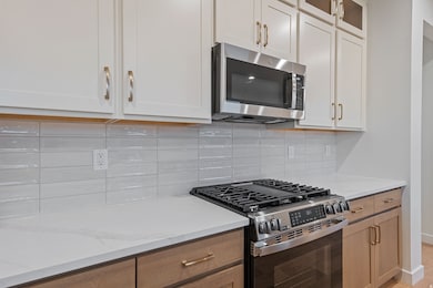 Kitchen featuring stainless steel appliances, decorative backsplash, light stone counters, glass insert cabinets, and white cabinetry