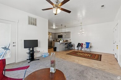 Living area with light carpet, ceiling fan, and light wood-style flooring