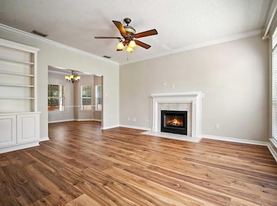Unfurnished living room with a textured ceiling, a chandelier, wood finished floors, a tile fireplace, and a ceiling fan