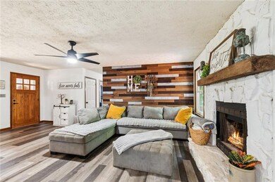 Living room featuring a stone fireplace, wood walls, wood finished floors, ceiling fan, and a textured ceiling