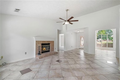 Unfurnished living room featuring ceiling fan, light tile patterned floors, a fireplace, a textured ceiling, and high vaulted ceiling