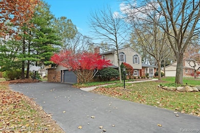 View of front facade featuring brick siding, a garage, a chimney, and driveway