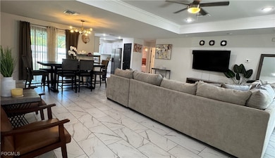 Living room with light marble finish floors, crown molding, a tray ceiling, a chandelier, and a ceiling fan