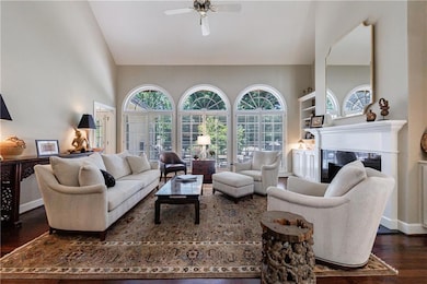 Living room with wood finished floors, a glass covered fireplace, a ceiling fan, and high vaulted ceiling
