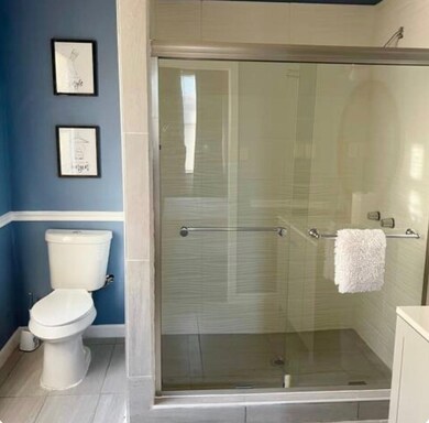 Bathroom featuring toilet, baseboards, a stall shower, and tile patterned flooring