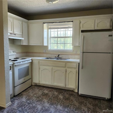 Kitchen with fridge, stove, tile countertops, extractor fan, and white cabinetry